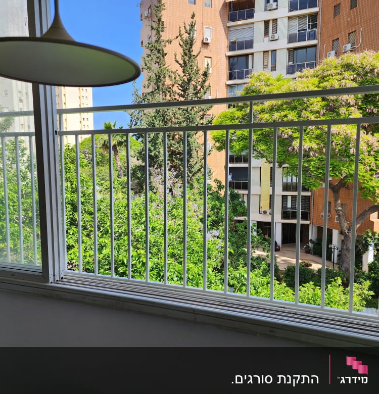 חלון עם מסגרת מתכת ונוף של עצים ובניינים